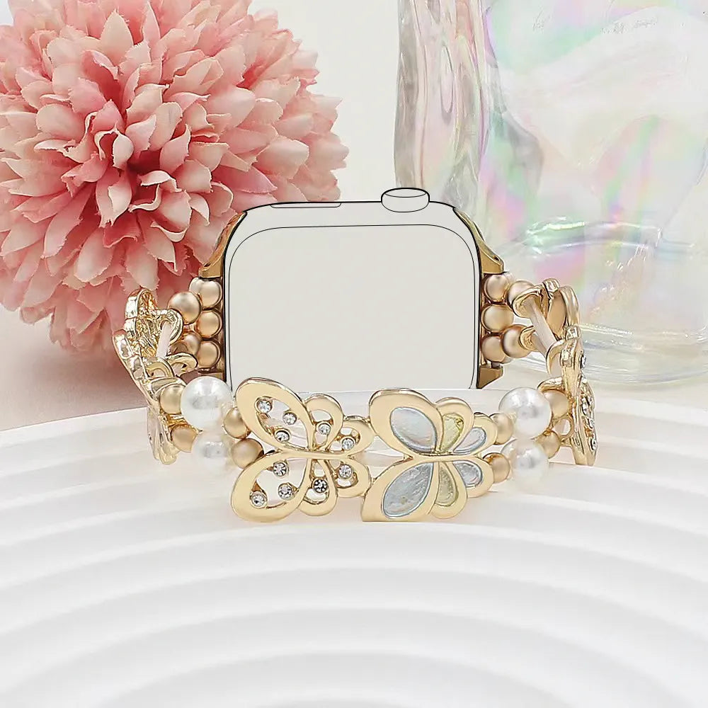Gold bracelet with butterfly design on a white surface with a pink flower in the background