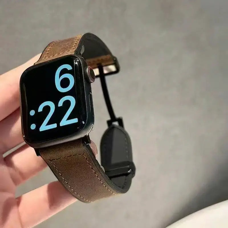 Smartwatch with a brown leather strap held in a hand against a neutral background