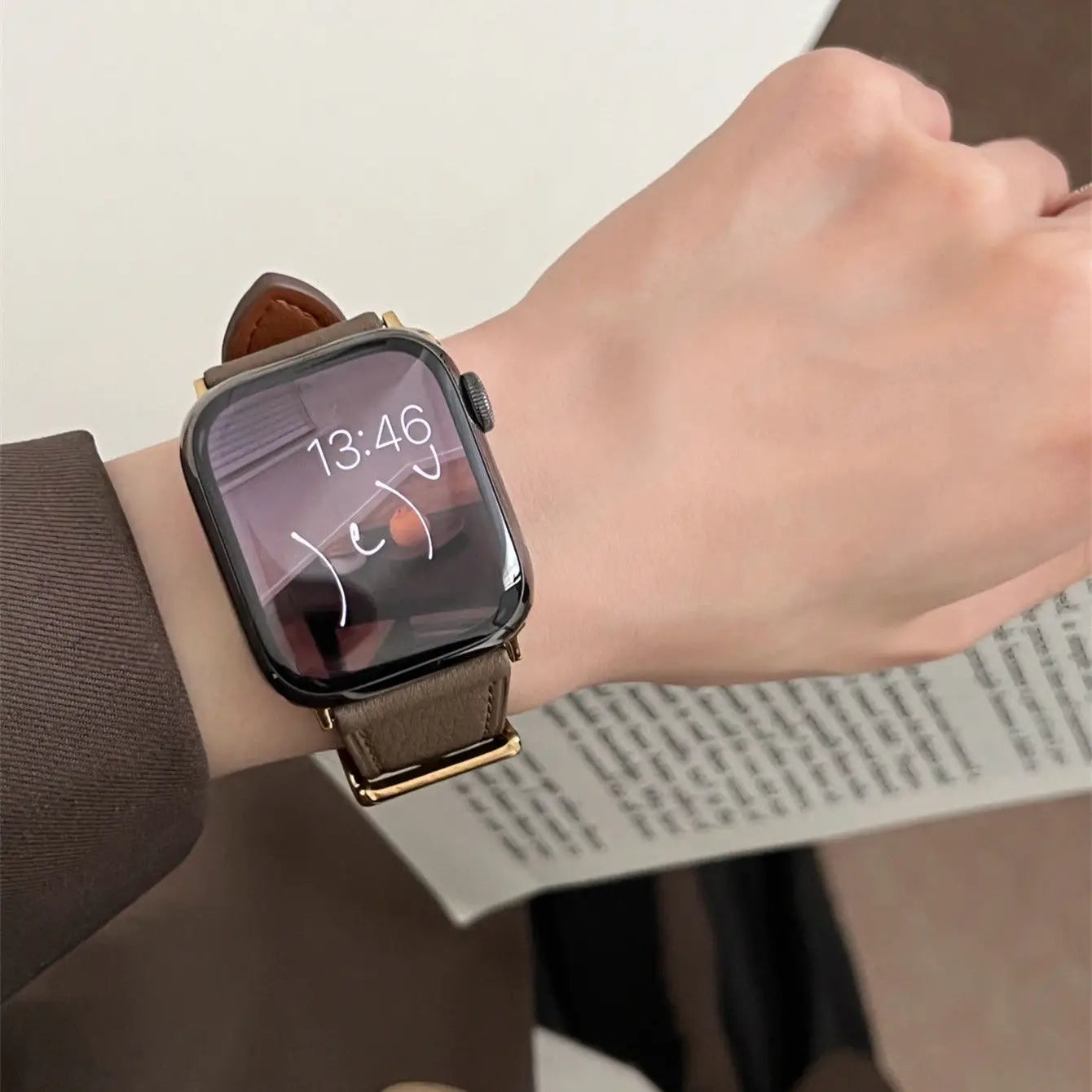 Smartwatch with a brown leather strap on a wrist, displayed on a plain background.