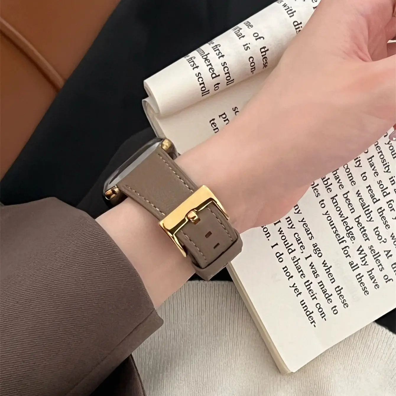 Person wearing a watch with a brown strap and gold buckle on a book background