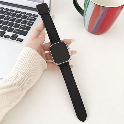 Person holding a black smartwatch on a desk with a laptop and colorful mug in the background