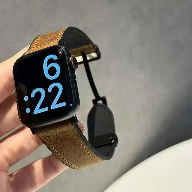 Smartwatch with a brown leather strap held in a hand against a gray background
