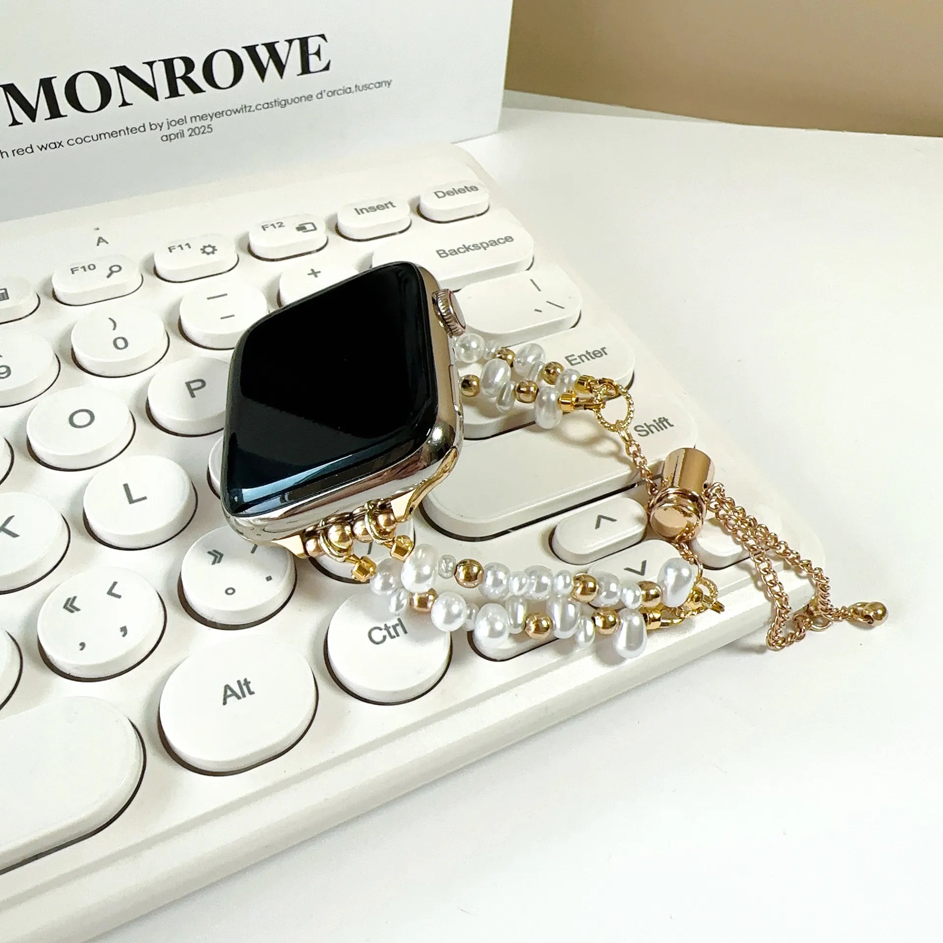 Black phone case with gold and pearl accents on a keyboard, featuring the brand 'Monrowe'.