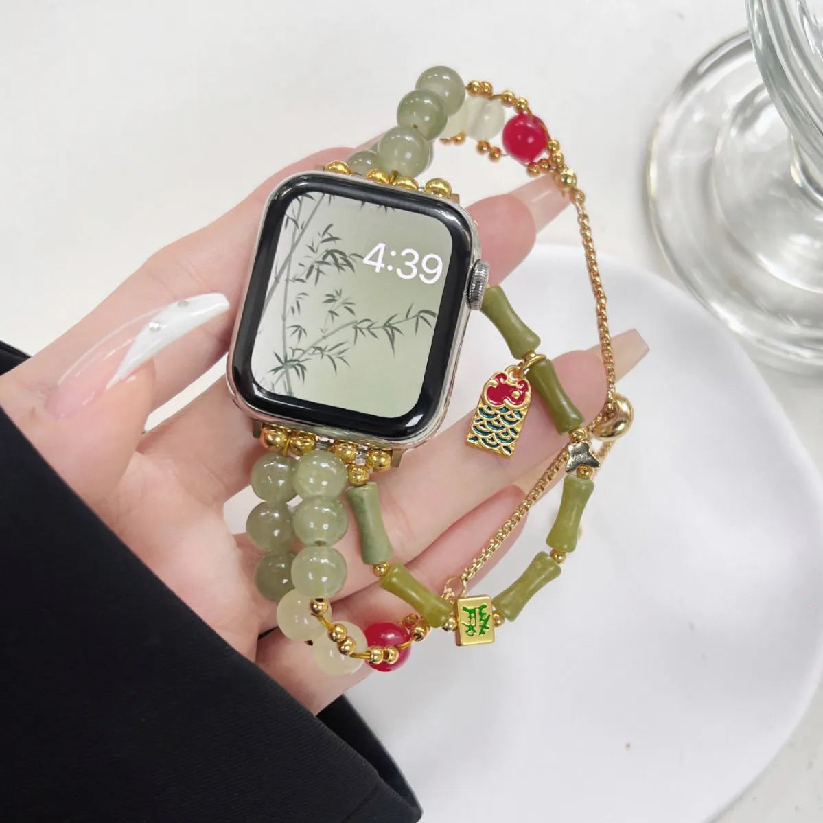 Smartwatch with a decorative beaded strap held by a hand on a white surface