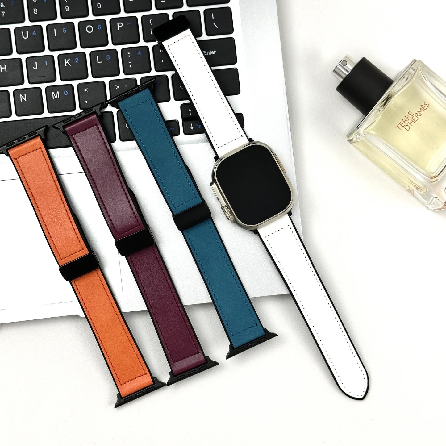 Set of colorful watch straps on a laptop keyboard with a perfume bottle in the background