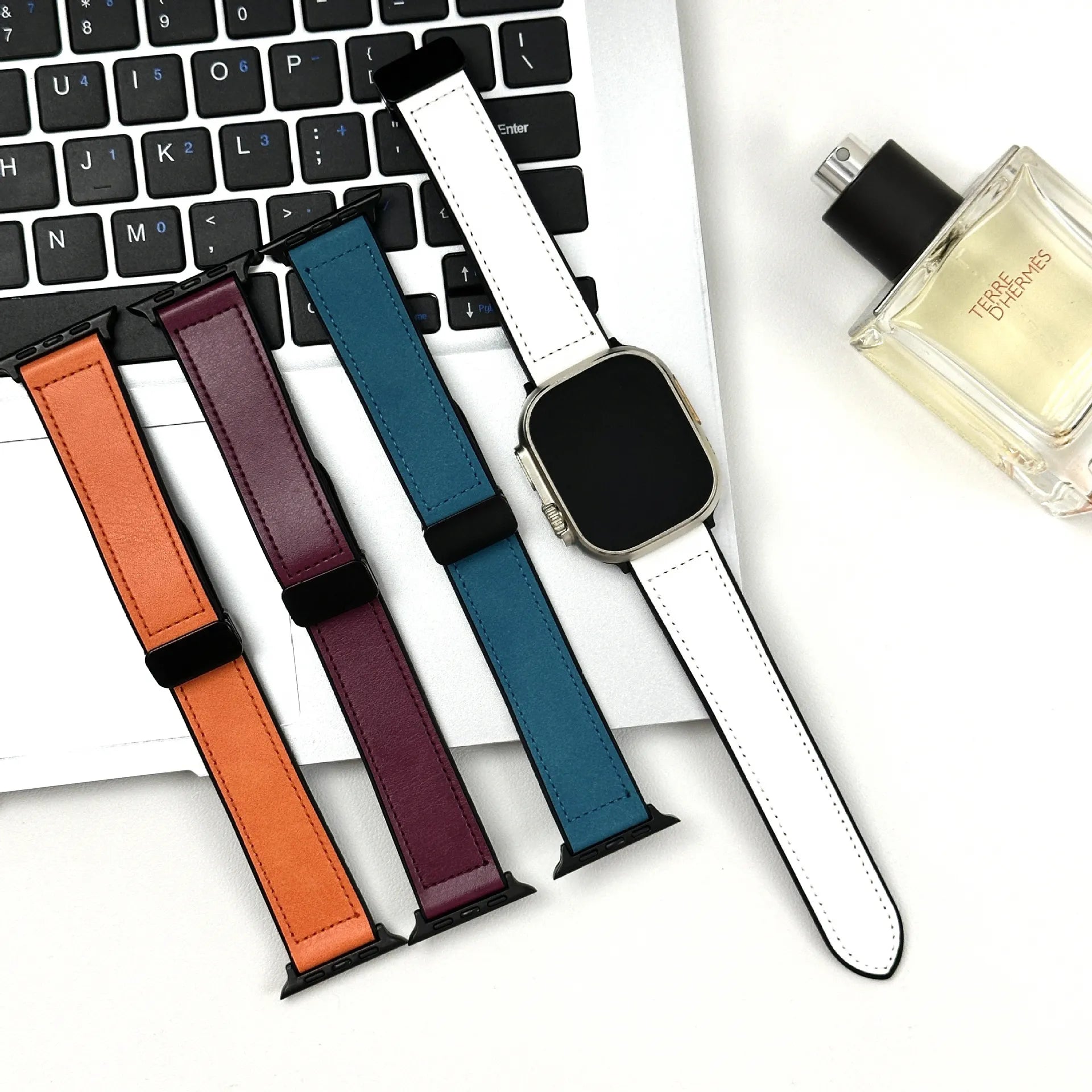 Set of colorful watch straps on a laptop keyboard with a perfume bottle in the background