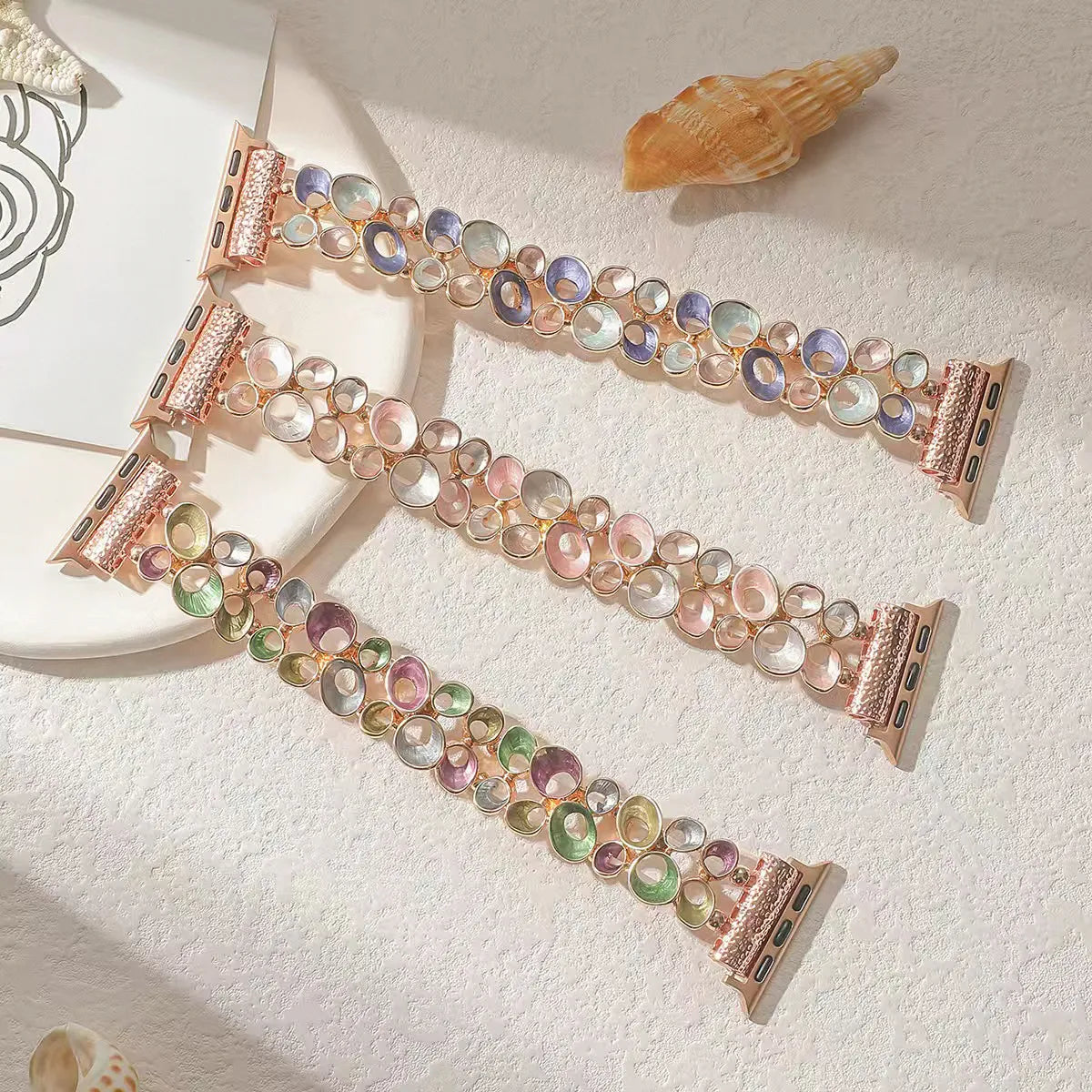 Multicolored gemstone watch band with rose gold clasp on a textured surface with shells.