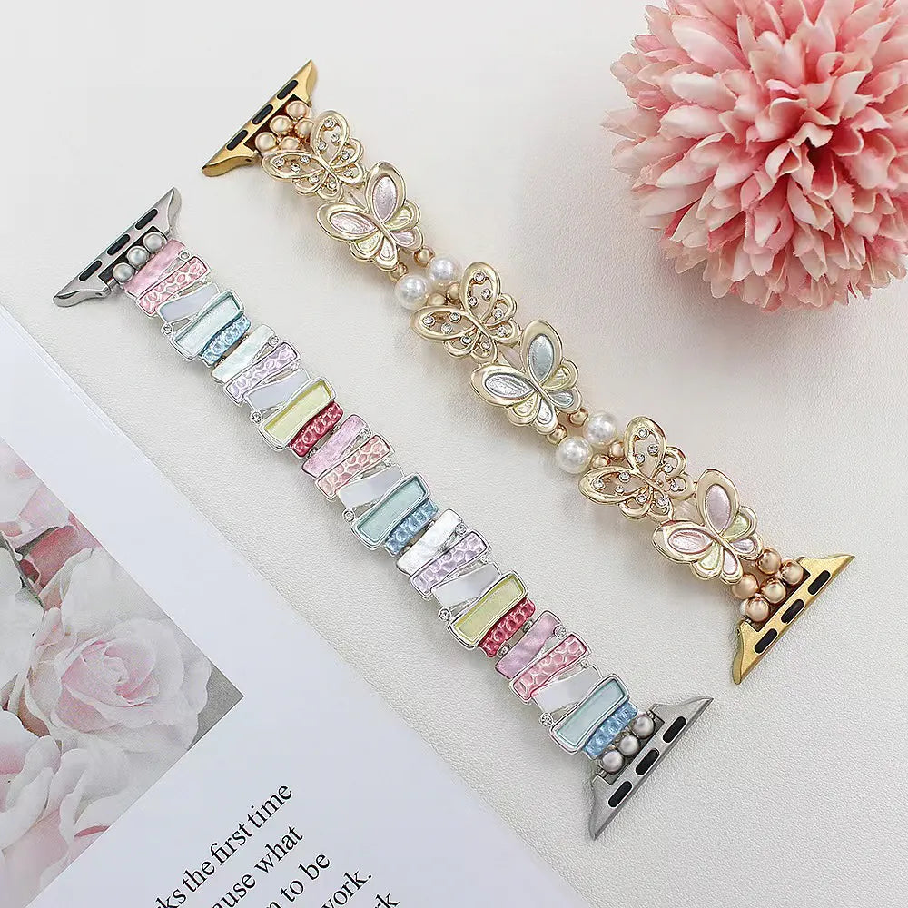 Decorative watch straps with butterfly and bow designs on a white surface with a pink flower.