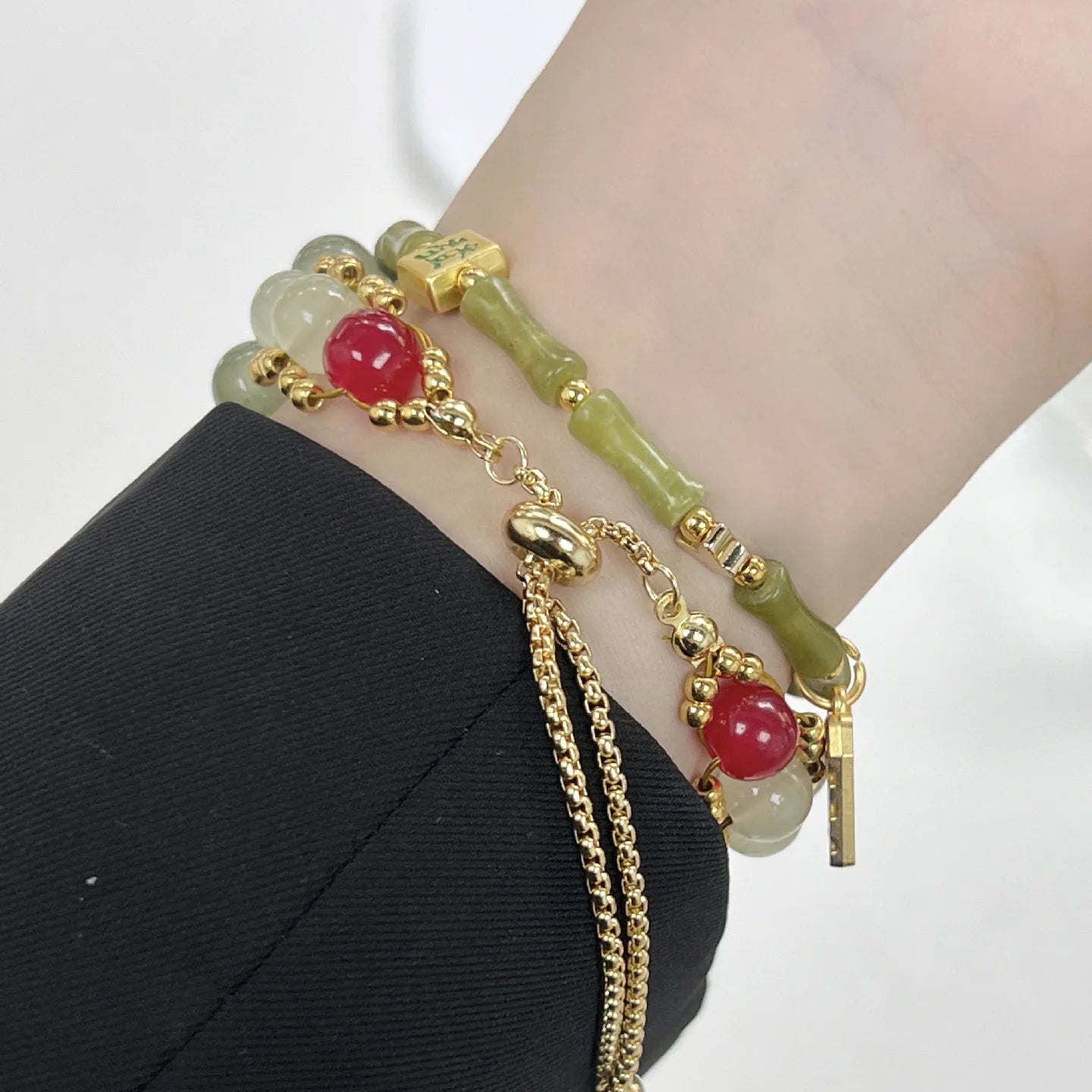 Bracelet with green beads and gold chain on a wrist against a white background