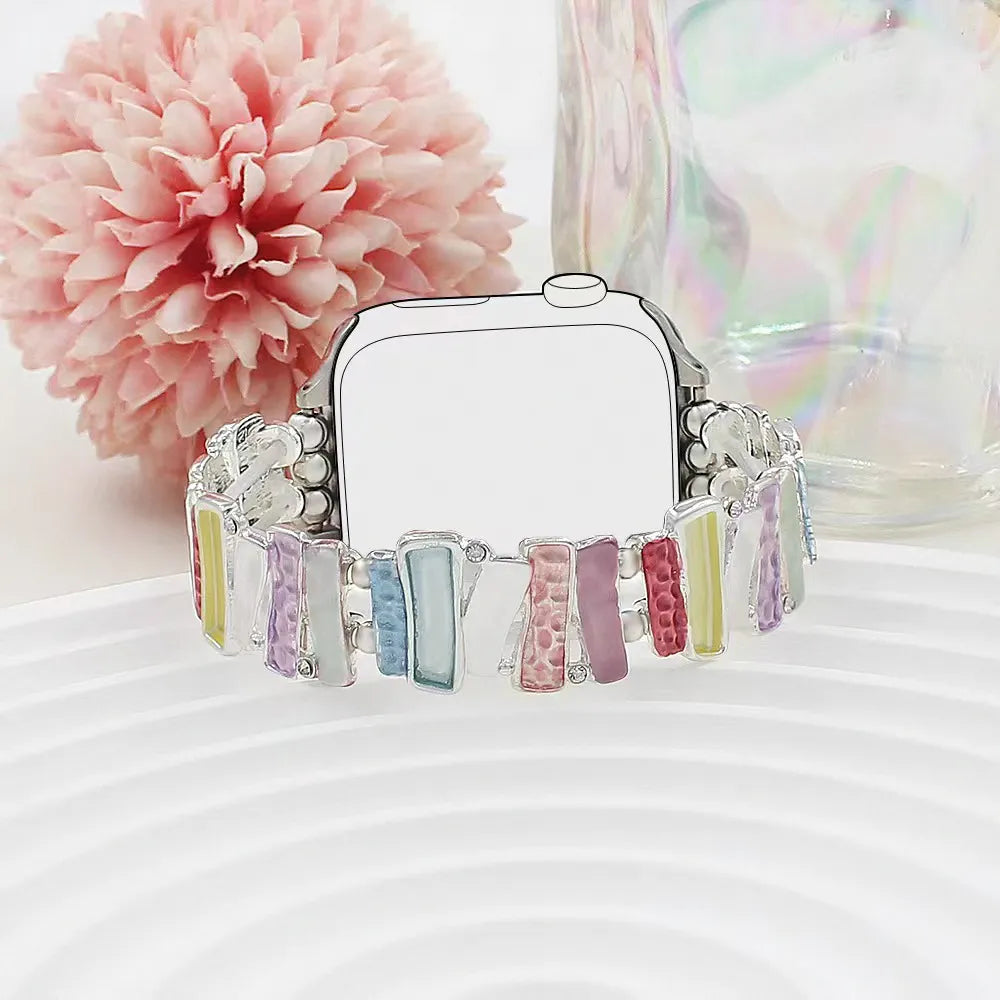 Smartwatch with colorful band on a white surface with a pink flower in the background