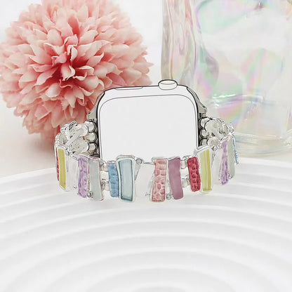 Smartwatch with colorful band on a white surface with a pink flower in the background