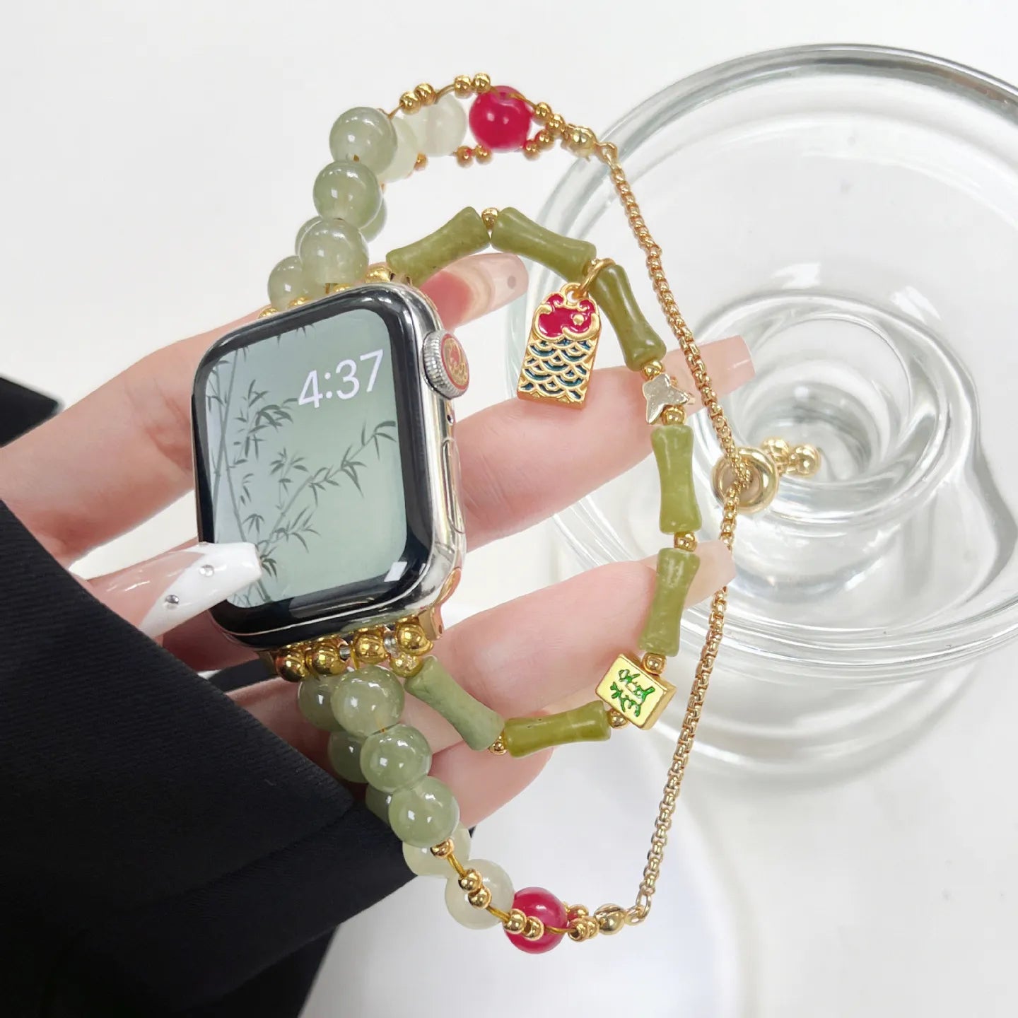 Smartwatch with a decorative green beaded strap held by a hand on a white background