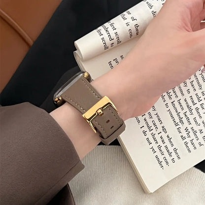 Person wearing a watch with a brown strap and gold buckle on a book background